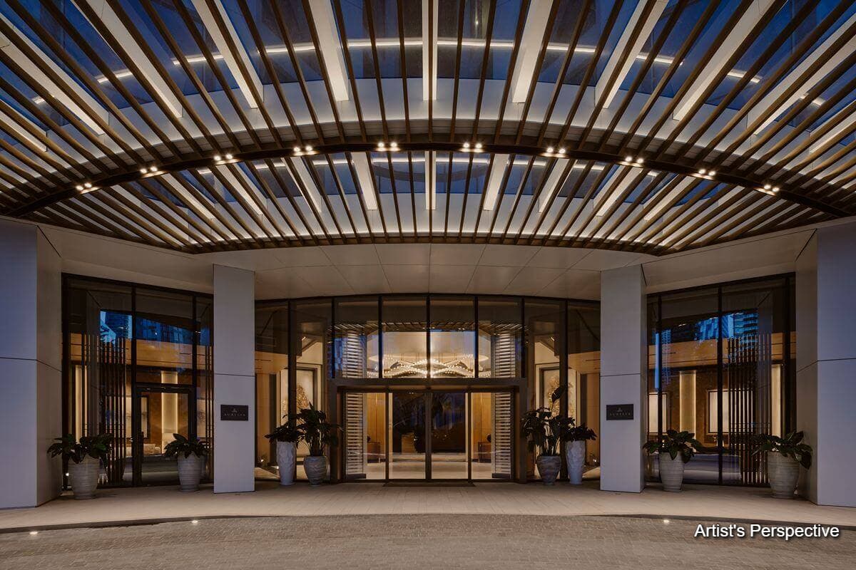 Artist’s rendering of an elegant residential building entrance with a covered driveway, warm lighting, and landscaped surroundings