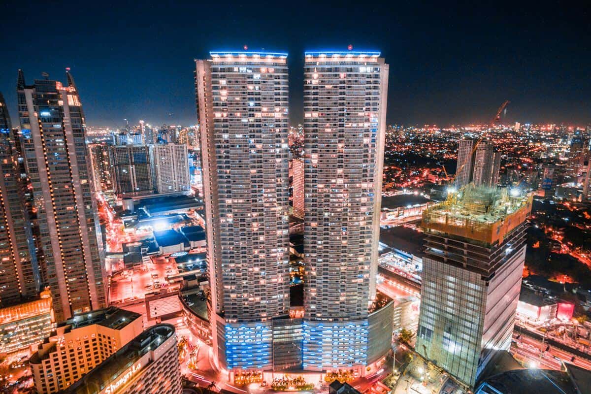 Illuminated twin residential towers in Metro Manila surrounded by commercial buildings and city lights at night